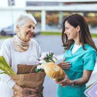 aide and senior woman smiling while holding a bag of grocery